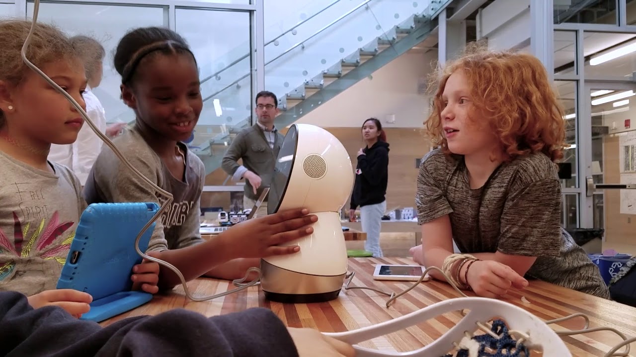Three children at school sit at a table with a Jibo robot.