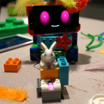 Children playing with tablets to program their robots, which are made out of Legos and Android phones with smiley faces programmed onto them.