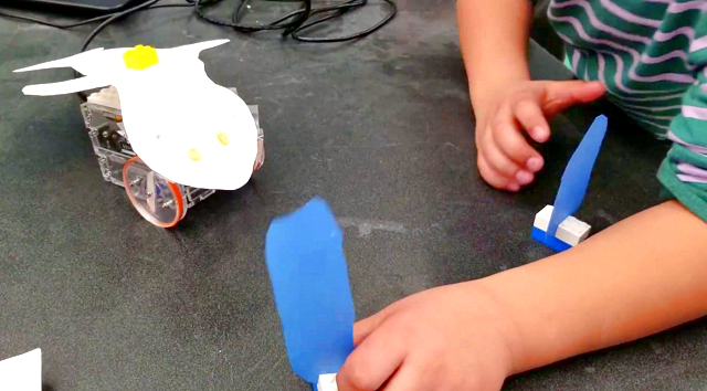 Child plays with small homemade robot with a cutout of a whale pasted on top of it.