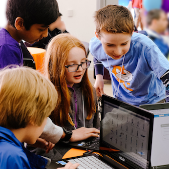 A group of children gathered around a laptop, programming in Scratch