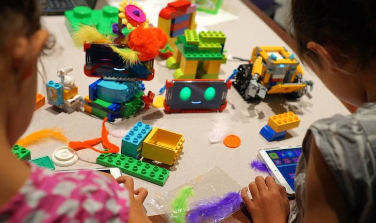 Children playing with tablets to program their robots, which are made out of Legos and Android phones with smiley faces programmed onto them.