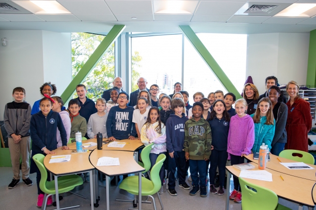 A large group of children and their teachers stand smiling for a picture in a classroom.