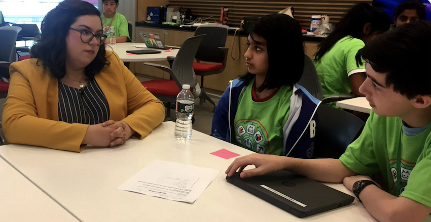 A researcher talks to two middle school students while sitting at a table.